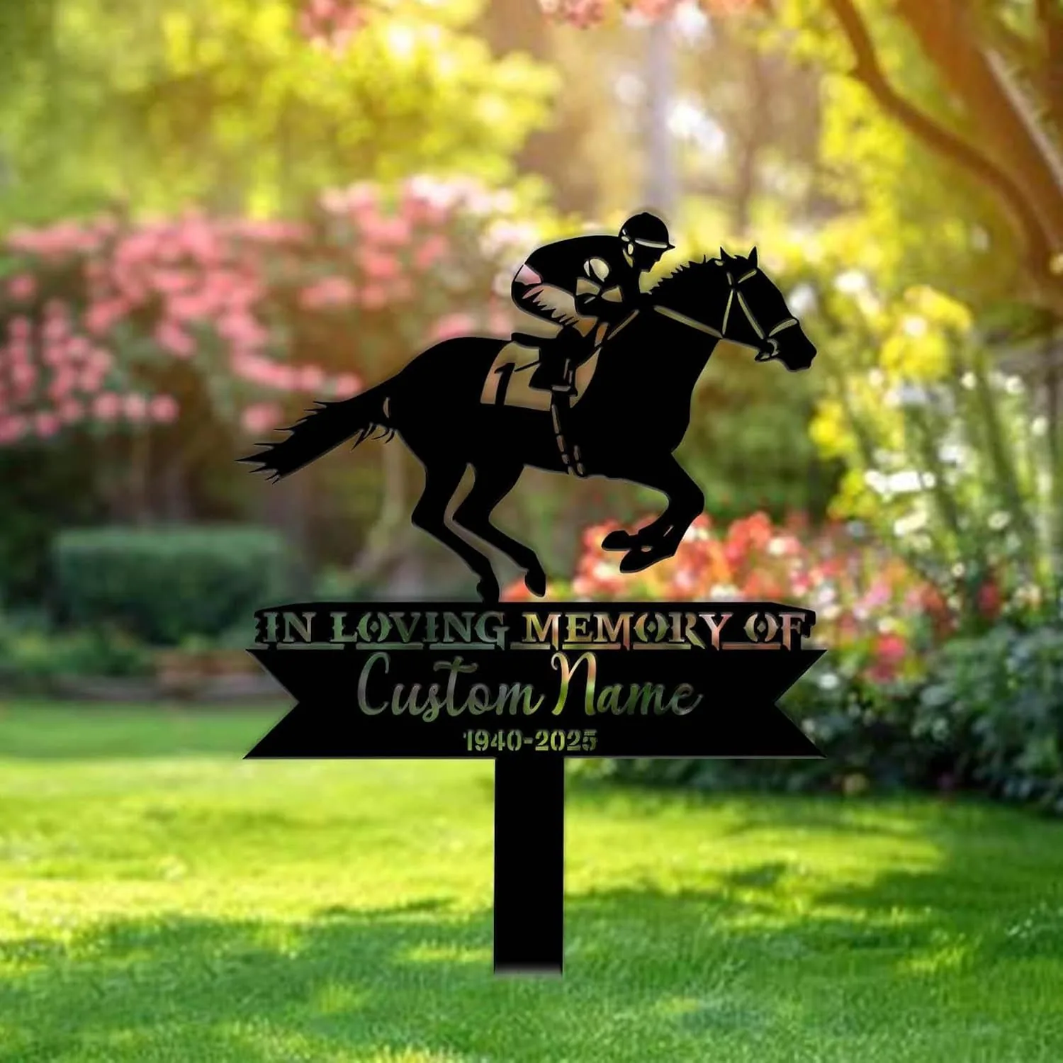 Black metal memorial yard sign showing a jockey on a racehorse above text 'IN LOVING MEMORY OF' and 'Custom Name 1940-2025' staked in a sunlit garden