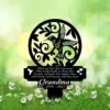 Black circular metal memorial plaque with a hummingbird and leaves, mounted in a daisy-filled lawn; text reads a poem and “Grandma 1940 - 2023”