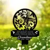 Black metal memorial garden stake with hummingbird and floral cutout, poem text and inscription “Grandma 1940 - 2023” against sunlit grassy field with white flowers