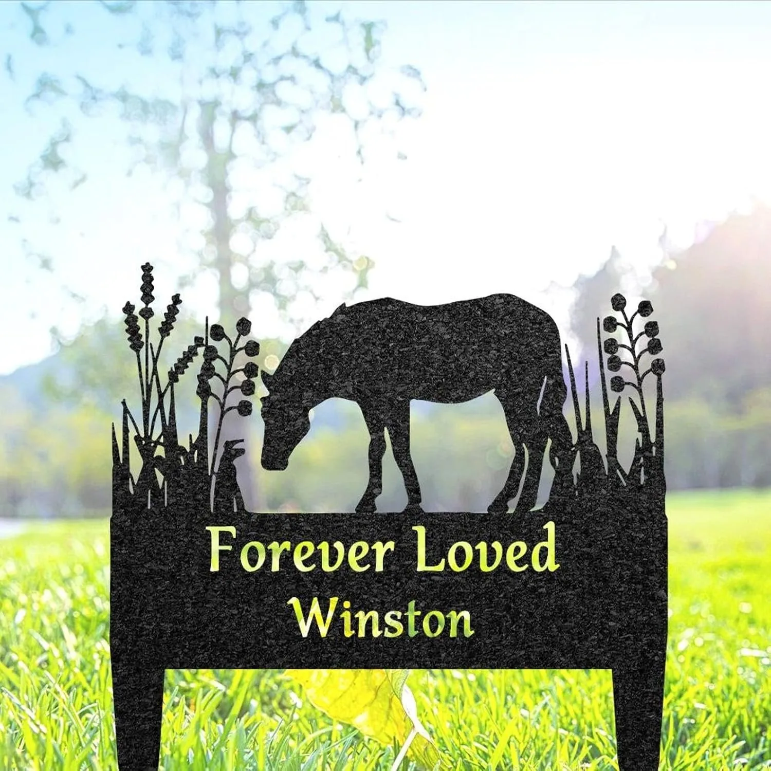 Black metal grave marker silhouette of a grazing horse with floral accents and yellow text reading "Forever Loved Winston" set in sunlit grass
