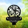 Black metal memorial garden stake with a hummingbird and floral cutout, inscription reading a short poem and 'Grandma 1940 - 2023', placed in grassy field with yellow flowers