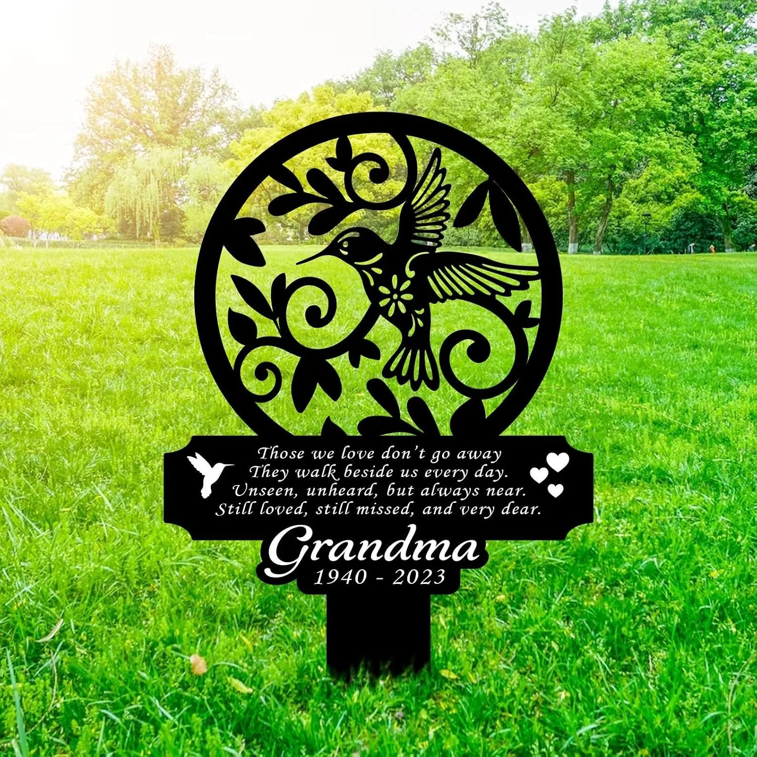 Black metal memorial garden stake in grass featuring a circular hummingbird and vine cutout and plaque reading 'Those we love don't go away... Grandma 1940 - 2023'