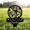 Black metal memorial garden stake in grass with a hummingbird cutout, decorative swirls and text reading “Those we love don’t go away... Grandma 1940 - 2023”