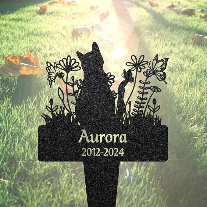 71-1 Black metal garden memorial stake shaped like a cat silhouette among flowers with the name "Aurora" and dates "2012-2024" set against sunlit grass
