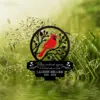 Black circular memorial plaque with a red cardinal perched on branches, text reading "When cardinals appear a Loved one is near" and name "Lauren Millier 1953 - 2024" against a dewy green grass background