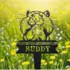 81-1 Black metal memorial stake in grass with cartoon guinea pig holding a heart and text ‘In Loving Memory of Buddy’ among yellow wildflowers