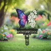 Garden memorial sign in a lawn showing a colorful galaxy-patterned butterfly and white flowers above text reading "TERESA'S GARDEN" and date "1975 - 2025"