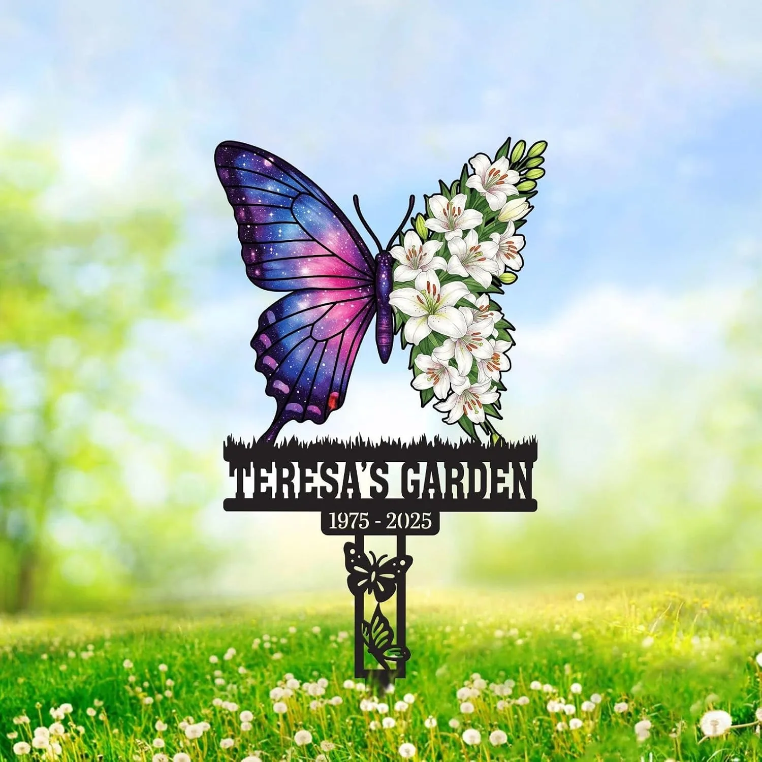Garden memorial stake shaped like a butterfly with one wing galaxy-purple and the other wing made of white lilies, text 'TERESA'S GARDEN' and dates '1975 - 2025' against a sunny grassy background