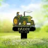 Garden memorial sign with a green tractor illustration and the text "In Loving Memory Of DADDY 1959 - 2025" against a sunny meadow background