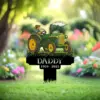 Garden memorial sign with a green tractor illustration and text “In Loving Memory Of DADDY 1959 - 2025” staked in a flowered lawn