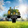 Memorial yard sign with a green tractor illustration and farmer, text reading "In Loving Memory Of DADDY 1959 - 2025" placed in a sunlit grassy field