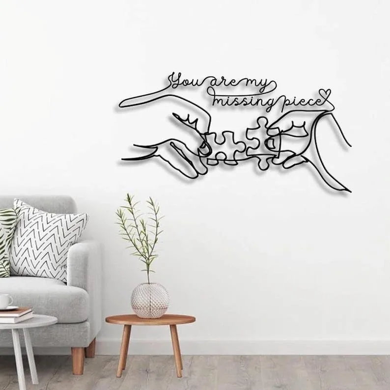 Minimal living room wall art showing two hands connecting puzzle pieces with script text 'You are my missing piece' above, black metal silhouette over white wall
