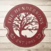 style-19.-Oak-Tree-Couple-1 Red circular metal family name sign reading "The Hendersons" with a tree cutout and "EST. 1995" on a light wood background