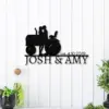 style-20.-Farmer-Tractor-Couple-2 Black metal wall sign of couple kissing on a tractor above text 'JOSH & AMY' and 'est. 4.10.2019' mounted on white shiplap wall with potted plants