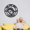 Black circular metal wall art with two wolves and text 'MR AND MRS' and last name 'LADOUGH' hanging on white brick wall above an elderly couple sitting on a yellow couch
