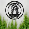 Black metal wall sign reading 'MR & MRS MARKSON EST. 2024' showing a couple kissing on bicycles, mounted on a light wall above green plants