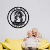 style-24.-Mountain-Bike-Couple-2 Black circular metal wall sign reading “MR & MRS” and “EST. 2024 MARKSON” with a couple on bicycles, hung on white brick above an elderly couple on a yellow sofa