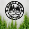 style-25.-Deer-Couple-1 Black circular metal wall sign reading 'Morris & Mary', '60 Years together', 'Est. 1963' with deer and pine tree silhouette, mounted on a light wall above green plants