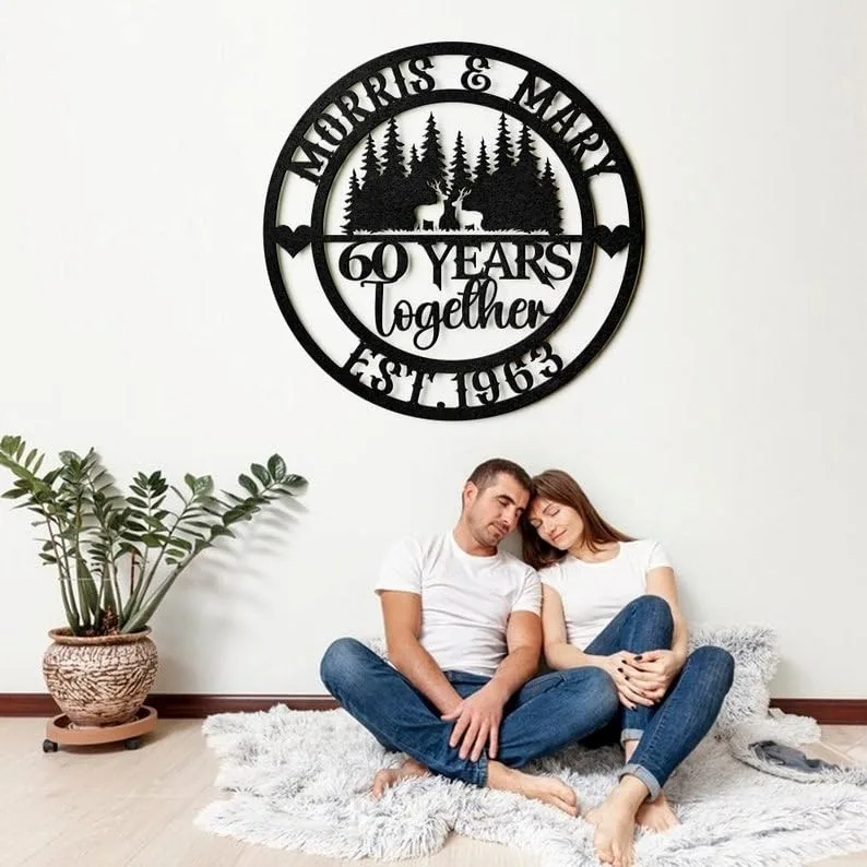 style-25.-Deer-Couple-2 Black circular wooden wall sign reading "Morris & Mary 60 Years Together Est. 1963" with forest and deer design hung above a couple sitting on a rug in a bright living room