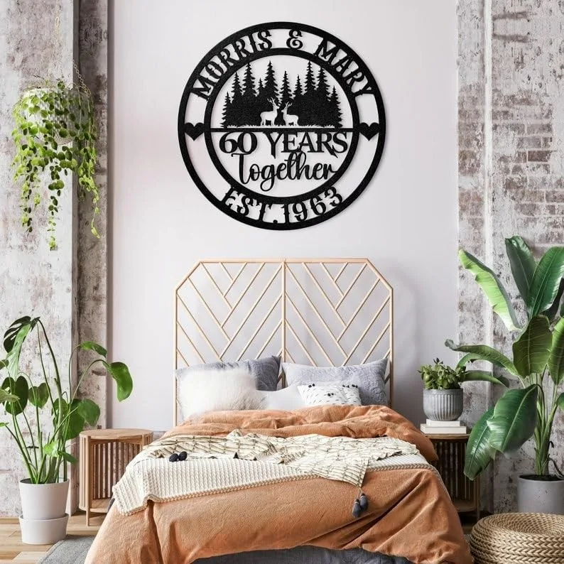 style-25.-Deer-Couple-3 Black circular metal wall sign reading “Morris & Mary 60 Years Together Est. 1963” with deer and trees, hanging above a boho bedroom bed with plants