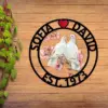 Round wooden wall sign with black cutout ring reading 'SOFIA ♥ DAVID' and 'EST. 1973' surrounding two white doves perched on pink cherry blossoms, displayed on wooden plank background with ivy on left