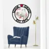 Round black wall sign reading "SOFIA ♥ DAVID EST. 1973" with two white doves and pink blossoms, hung above a blue velvet armchair and gold floor lamp in a minimalist room
