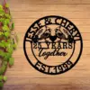 Black circular wooden sign on a wood plank wall reading "Jesse & Cheryl" at top, two cardinals facing a heart with "25 Years Together" in center and "Est. 1999" at bottom