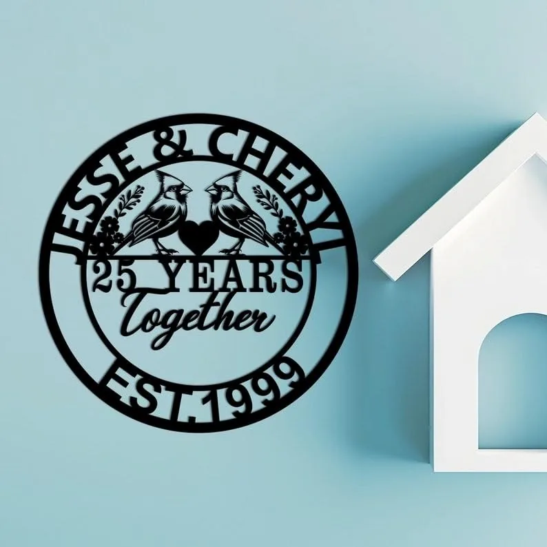 Black circular wall plaque reading "Jesse & Cheryl" with two cardinals, "25 Years Together" and "EST. 1999" mounted on a light blue wall beside a white decorative house shelf