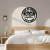Black circular metal wall sign reading "25 Years together" with two birds and "EST 1999" hung above a modern wooden bed in a minimalist bedroom