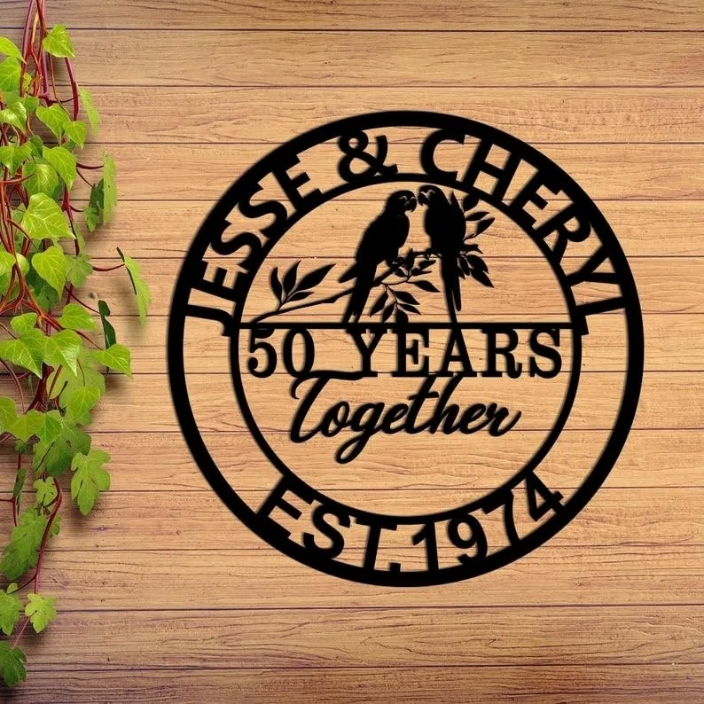 style-29.-Parrot-Couple-1 Black circular wooden sign on a wood plank background reading "Jesse & Cheryl" at top, "50 Years Together" center with two parrots on a branch, "Est. 1974" at bottom