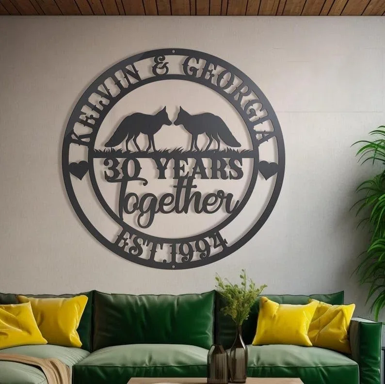 Round metal wall sign reading “Kevin & Georgia 30 Years Together Est. 1994” with two fox silhouettes, mounted above a green sofa with yellow pillows in a living room