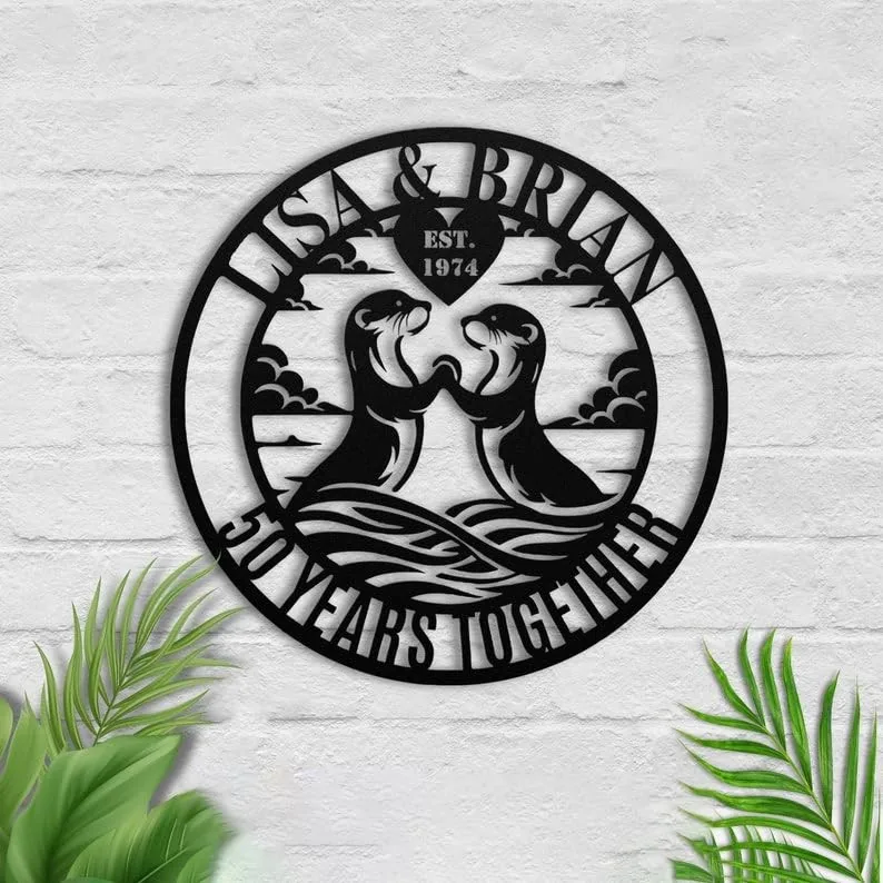 style-32.-Otter-Couple-1 Black metal wall sign on white brick reading “Lisa & Brian” and “50 Years Together” with two otters touching paws and a heart marked “Est. 1974,” surrounded by tropical leaves