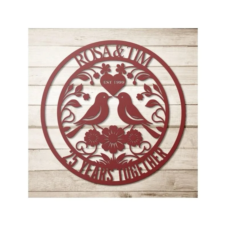 Red circular wooden wall sign with two birds facing each other, floral vines, a heart labeled "EST 1999", and names "ROSA & TIM" above with "25 YEARS TOGETHER" curved along the bottom, on whitewashed wood background