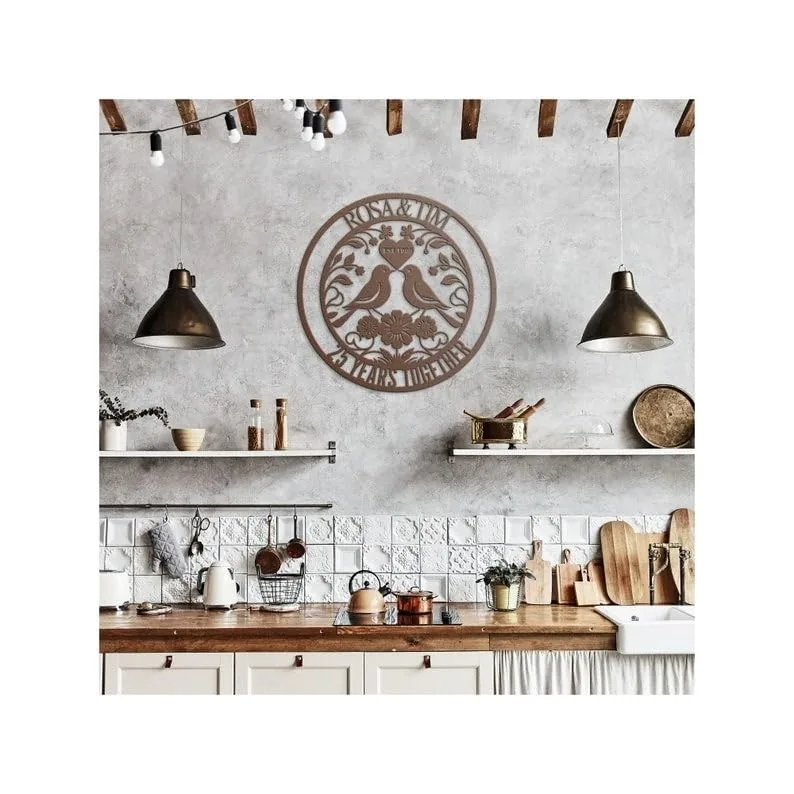 Rustic kitchen wall with wooden round metal sign reading “ROSA & IVAN” above a wooden countertop, pendant lights, open shelves, cutting boards, kettle and plants