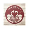 Round red wooden wedding sign on a whitewashed plank background reading "SAVE THE DATE" with date 08.10.2023, two swans forming a heart, floral heart and names "HANNA & TOMMY"
