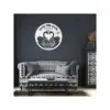Round white wooden 'Save the Date' wall sign with two swans forming a heart, wedding rings, date 08.10.2023 and names over a dark gray living room wall above patterned black-and-white sofa