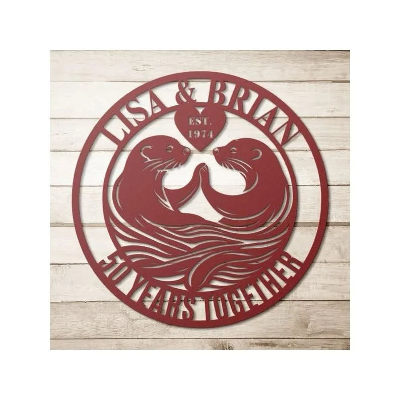 style-35.-Otter-Anniversary-2 Red circular metal wall sign with two otters facing each other, heart reading "EST. 1974," names "LISA & BRIAN" across top and "50 YEARS TOGETHER" along bottom, on whitewashed wood background
