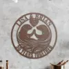 style-35.-Otter-Anniversary-3 Round metal wall sign with two otters facing each other, heart at top reading "EST. 1971", names "Lisa & Brian" along top and "50 Years Together" along bottom, hung on a textured gray wall above kitchen counter