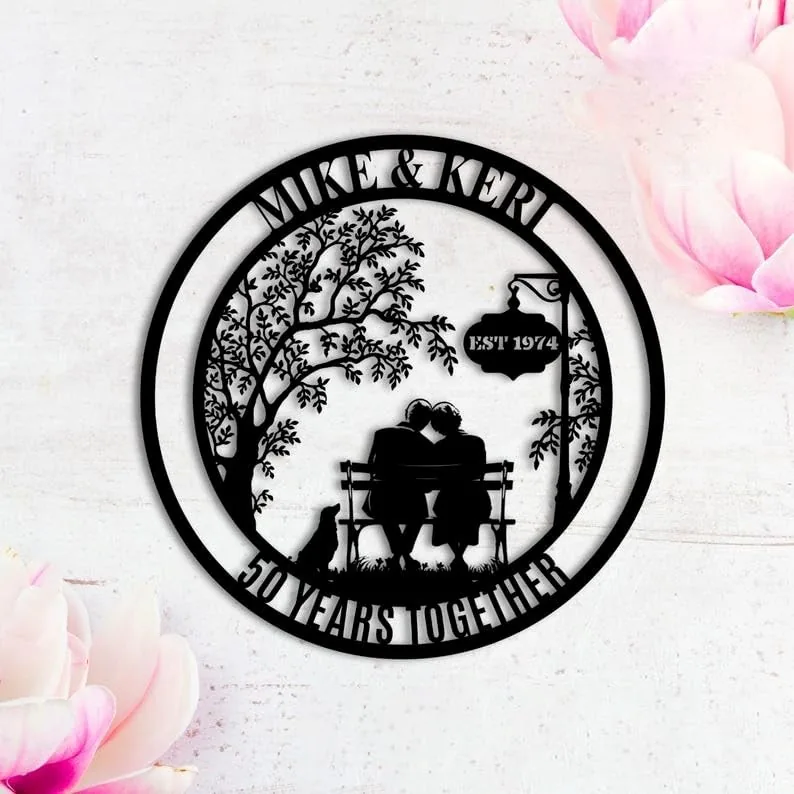 Black circular metal wall art showing couple on a bench with a dog, tree, sign reading EST 1974 and text 'MIKE & KERI' and '50 YEARS TOGETHER'
