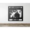 Black metal wall plaque reading "50th Anniversary Est. 1974" with silhouettes of a couple on a bench, a dog, tree, lamp, and names "Jim & Mary" hung on a white wall above a wooden shelf