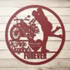 Round red metal wall art showing a motorcycle and a couple kissing, text 'Born To Ride Together FOREVER' and a heart with 'WILLIAMS 02.02.2005', on whitewashed wood background