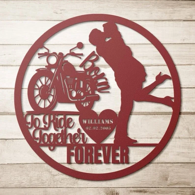 Round red metal wall art showing a motorcycle and a couple kissing, text 'Born To Ride Together FOREVER' and a heart with 'WILLIAMS 02.02.2005', on whitewashed wood background